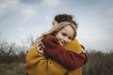 Lächelndes Mädchen umarmt Mutter vor dem Himmel - ALKF00125