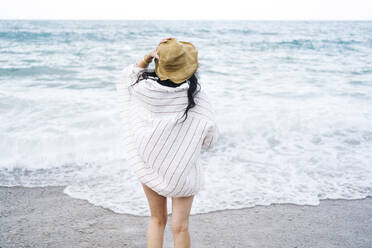 Frau mit Sonnenhut schaut am Strand aufs Meer - JJF00062