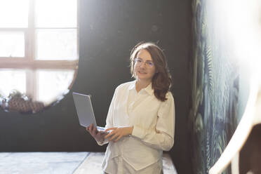 Smiling businesswoman standing with laptop - ONAF00407