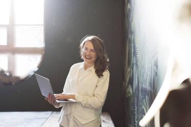 Happy businesswoman standing with laptop - ONAF00408