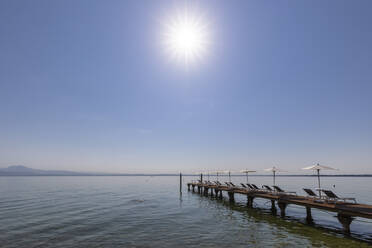Italien, Venetien, Bardolino, Sonne scheint über Liegestühle und Sonnenschirme auf einem Steg am Seeufer - FOF13438