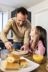 Lächelnder Vater, der seiner Tochter am Tisch das Frühstück serviert - WPEF07211