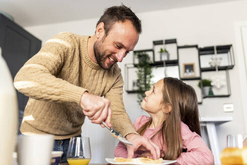 Happy father serving breakfast to daughter at table - WPEF07212