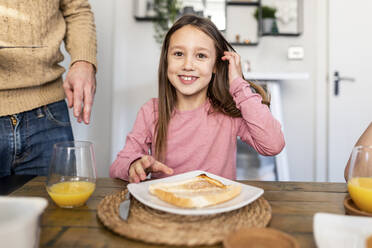 Smiling girl sitting with breakfast at table at home - WPEF07213