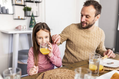 Glückliches Mädchen trinkt Saft mit Vater beim Frühstück zu Hause - WPEF07225