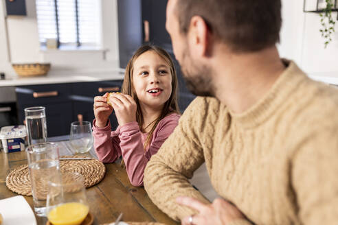 Glückliches Mädchen frühstückt mit ihrem Vater in der Küche sitzend - WPEF07236