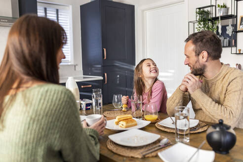 Fröhliches Mädchen mit Vater und Mutter beim Frühstück zu Hause - WPEF07240