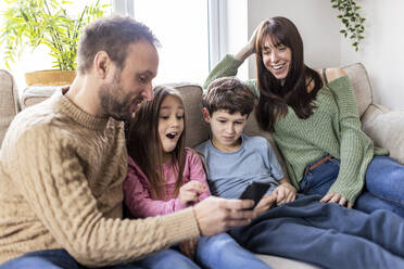 Happy family using smart phone on sofa at home - WPEF07244