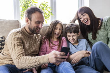 Cheerful family using smart phone on sofa in living room - WPEF07245