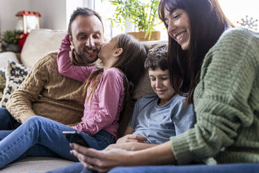 Happy mother using smart phone with son and girl kissing father at home - WPEF07247