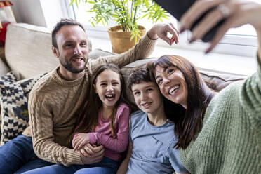 Glückliche Frau nimmt Selfie mit Familie auf Sofa zu Hause - WPEF07249