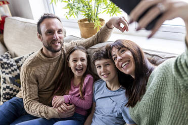 Happy woman taking selfie with family on sofa at home - WPEF07249