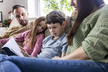 Junge, der mit seiner Familie zu Hause auf dem Sofa sitzt und ein Buch liest - WPEF07254