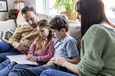 Girl reading book with family in living room at home - WPEF07257