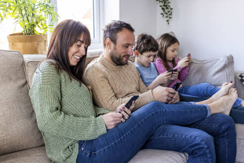 Glücklicher Mann und Frau mit Kindern, die zu Hause ein Smartphone benutzen - WPEF07261