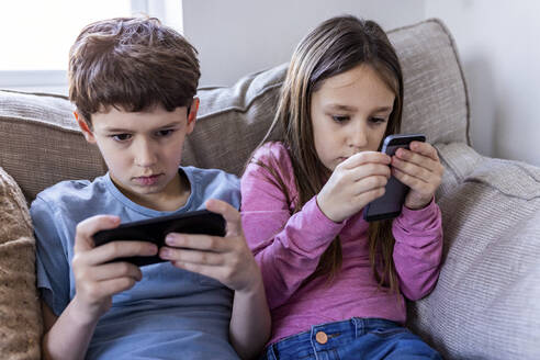 Mädchen und Junge benutzen ein Smartphone auf dem Sofa zu Hause - WPEF07262