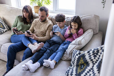 Familie mit Mobiltelefonen auf dem Sofa im heimischen Wohnzimmer - WPEF07263