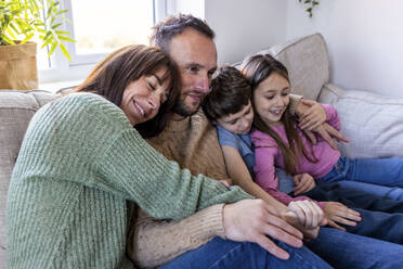Smiling woman embracing family on sofa at home - WPEF07265