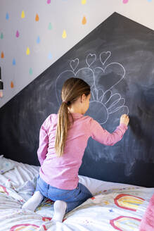Mädchen zeichnet mit Kreide auf Tafel im Schlafzimmer zu Hause - WPEF07273