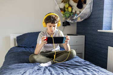 Junge mit Kopfhörern spielt ein Videospiel auf einem Tablet-PC - WPEF07276