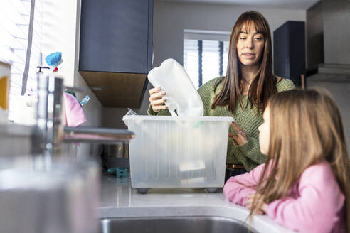 Woman recycling plastic bottles with girl standing in kitchen at home - WPEF07284