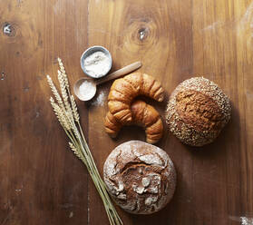 Freshly baked loaves of bread and croissants on wooden table - KSWF02288