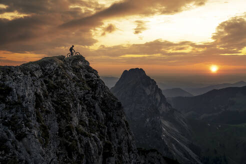 Mann mit Fahrrad auf dem Gipfel eines Berges bei Sonnenuntergang - MALF00422