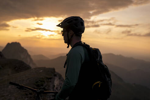 Mountainbiker unter bewölktem Himmel bei Sonnenuntergang - MALF00424