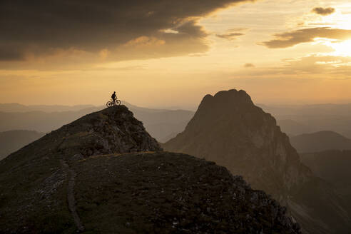 Mountainbiker mit Fahrrad auf dem Gipfel des Gipfels bei Sonnenuntergang - MALF00428