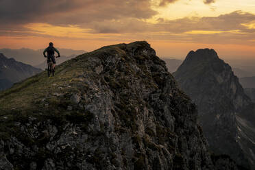 Mountain biker riding on summit at sunset - MALF00431