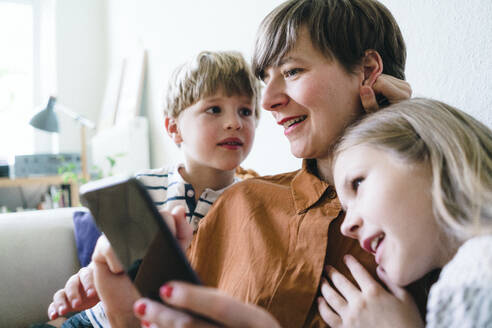 Lächelnde Frau teilt Smartphone mit Sohn und Tochter zu Hause - JOSEF16966