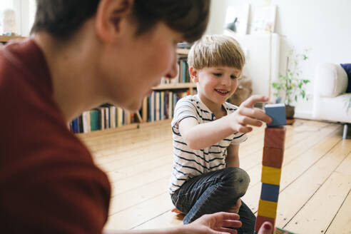 Smiling boy playing with toy blocks by mother at home - JOSEF16971