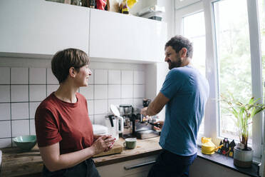 Woman talking to man preparing coffee in kitchen at home - JOSEF17004