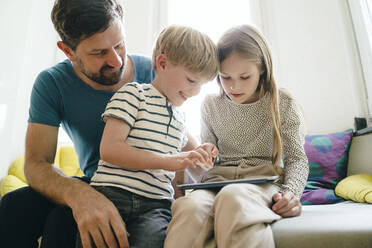 Lächelnder Sohn und lächelnde Tochter teilen sich einen Tablet-PC, der zu Hause steht - JOSEF17035