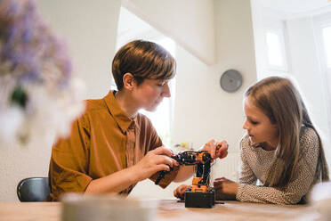 Mother explaining robotic model to daughter at home - JOSEF17045