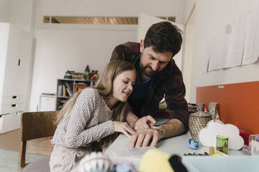 Father showing smart watch to daughter sitting at home - JOSEF17046