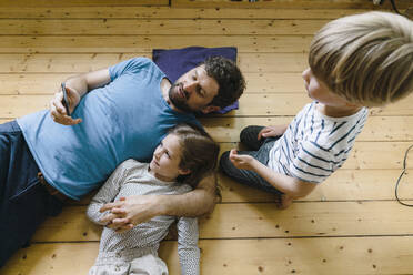 Father sharing smart phone with daughter and son lying on floor at home - JOSEF17056