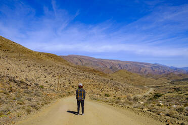 South Africa, Western Cape Province, Male hiker standing in middle of empty dirt road in Great Karoo - LBF03754