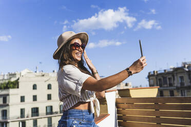 Glückliche Frau mit Hut nimmt Selfie an einem sonnigen Tag - JJF00144