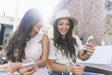 Happy woman with friend using smart phone on rooftop - JJF00151