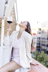 Smiling woman with glass of wine leaning on wall - JJF00196