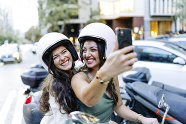 Cheerful woman wearing helmet taking selfie through smart phone - JJF00215