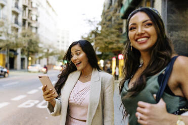 Überrascht Frau mit Smartphone mit Freund auf der Straße stehend - JJF00219