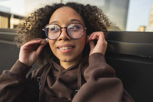 Young woman with curly hair wearing wireless in-ear headphones - JCCMF09437