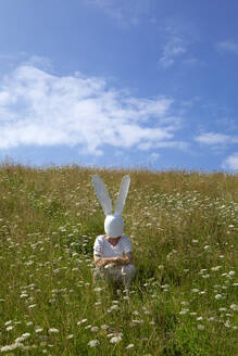 Frau mit Kaninchenmaske hockt auf einem Feld - PSTF01026