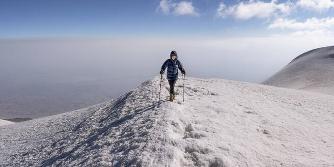 Senior woman hiking on snow covered mountain in front of sky at weekend - ALRF02005