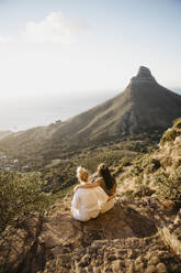 Freunde sitzen auf einem Felsen am Lion's Head Mountain bei Sonnenuntergang - LHPF01488