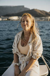 Smiling woman with eyes closed sitting on boat in sea - LHPF01494