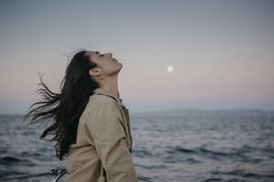Frau mit geschlossenen Augen am Meer bei Sonnenuntergang - LHPF01500