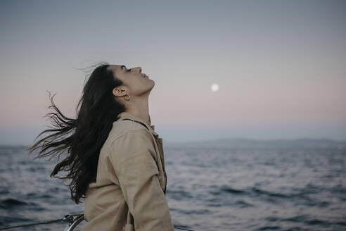 Woman with eyes closed by sea at sunset - LHPF01500